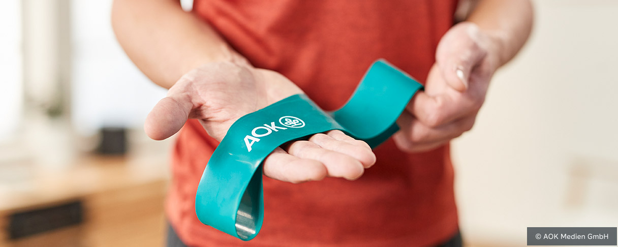 Person trainiert mit einem grünen Fitnessloop-Band im Wohnzimmer